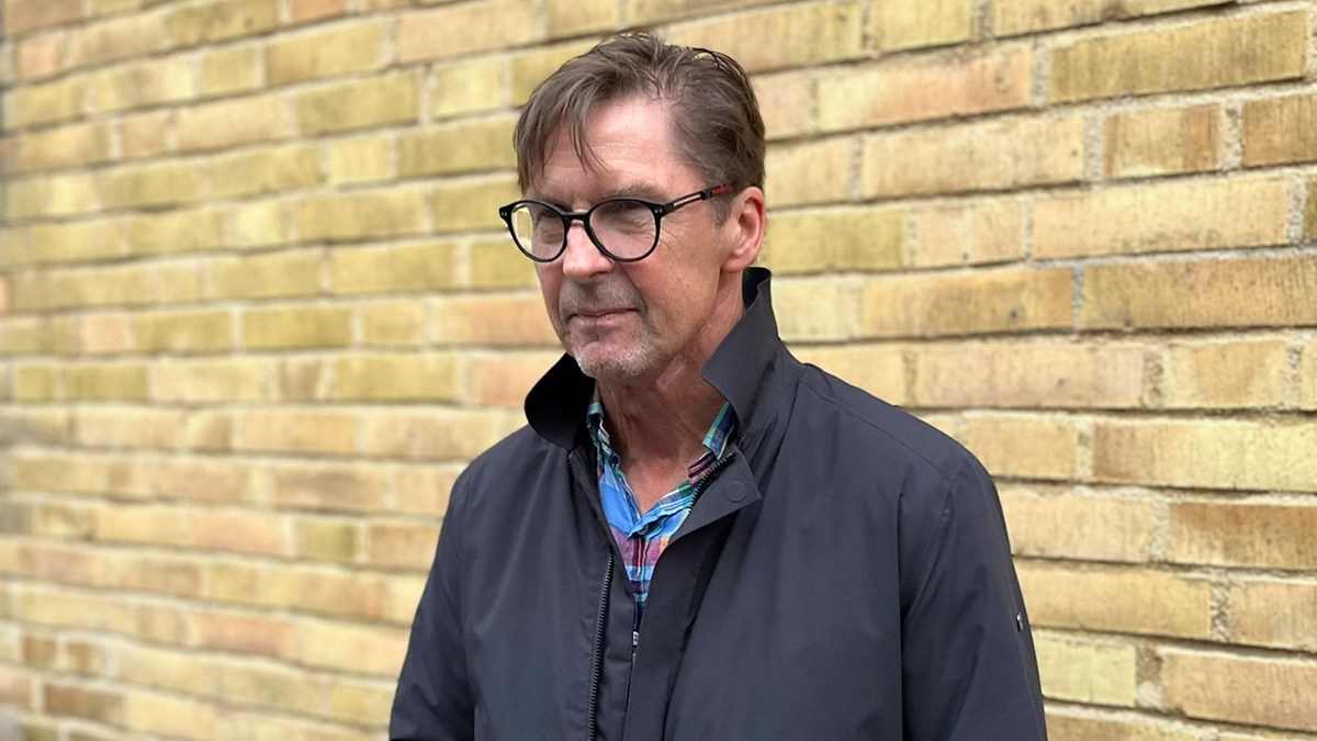  Per-Anders står framför en gul tegelvägg, han bär svarta glasögon och en rock.