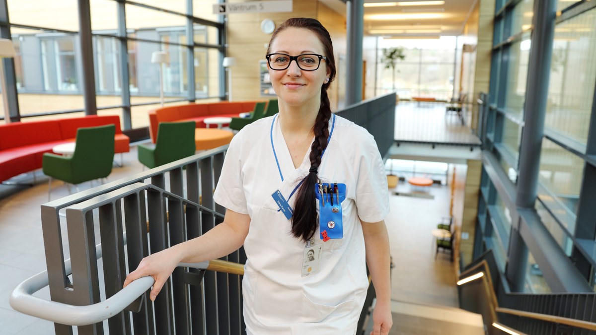 En sjuksköterska med lång mörk fläta och glasögon står längst upp i en trappa i ett sjukhus 