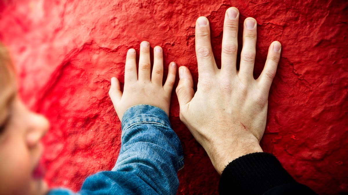 en barnhand och en vuxenhand bredvid varandra mot en röd bakgrund