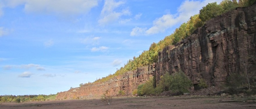 Stenbrottet på Kinnekulle. En hög stenvägg reser sig mot en blå himmel.