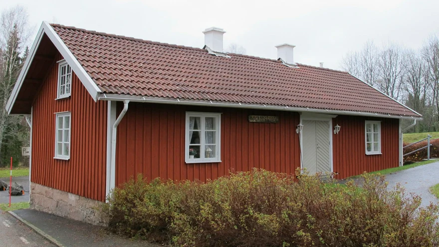 Röd stuga med tegeltak och texten sockenstuga på fasaden