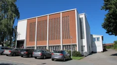 Ett stort vitputsat hus med tegelröda detaljer och ett kors över entrén