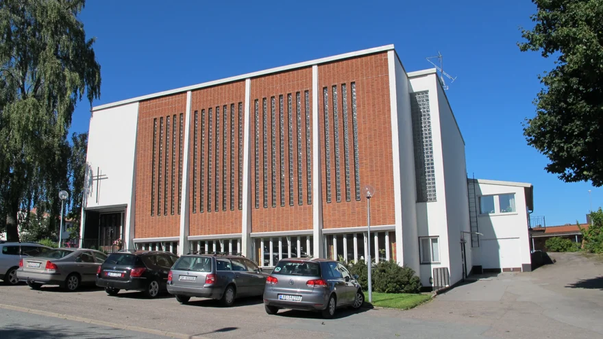 Ett stort vitputsat hus med tegelröda detaljer och ett kors över entrén