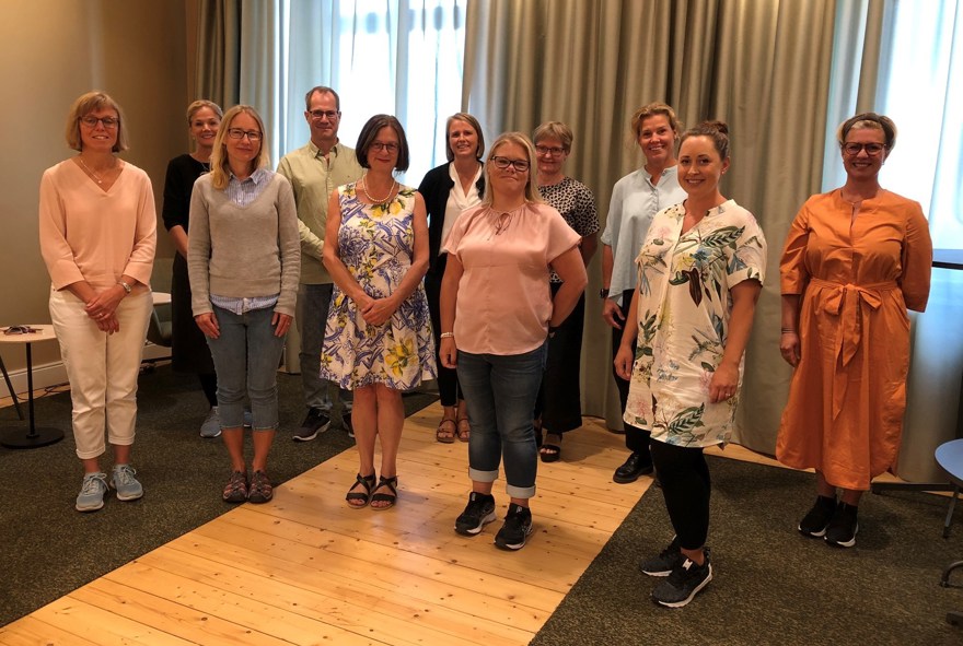 Elva kvinnor och män som står upp i ett konferensrum