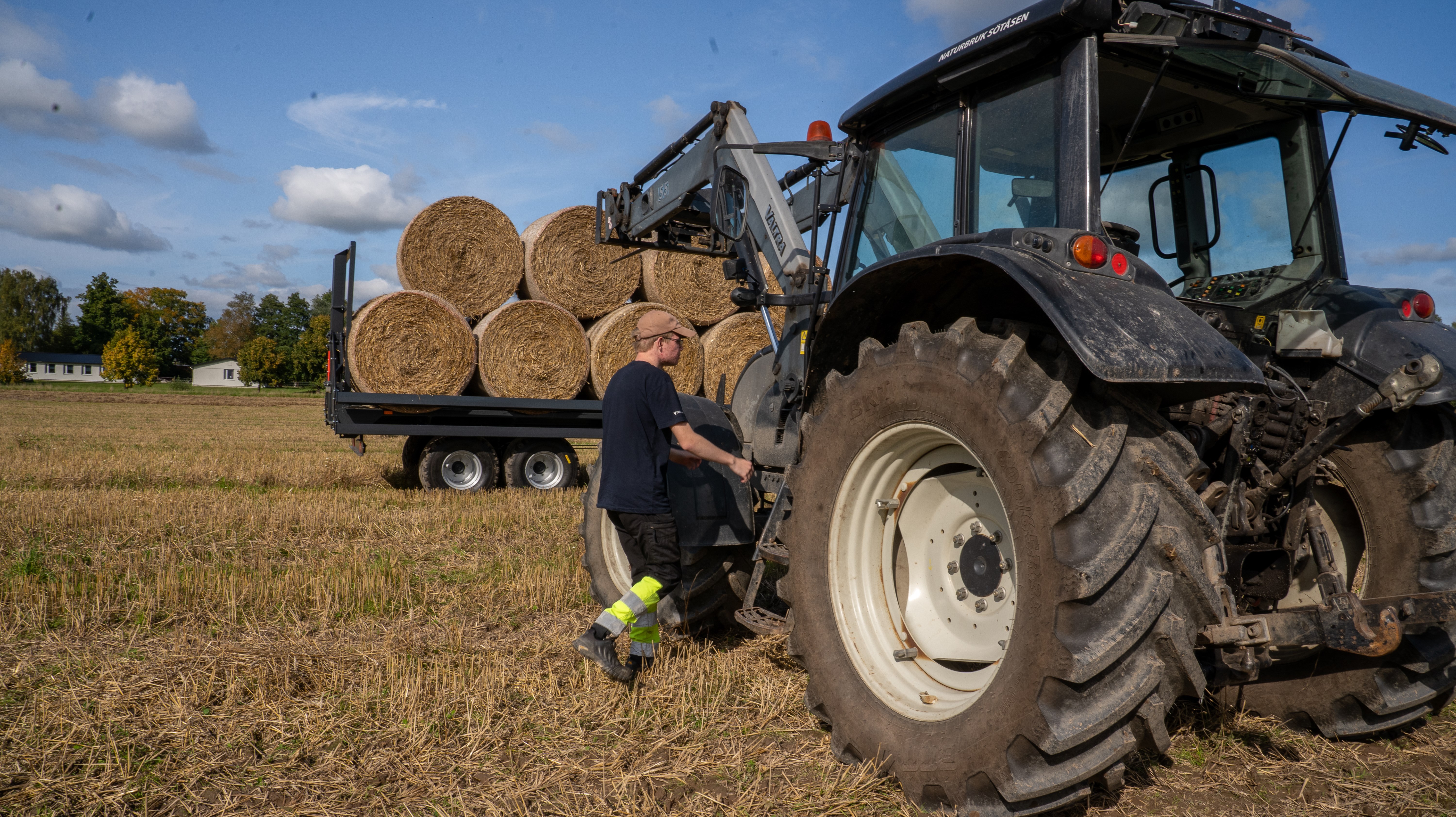 Elev är på väg mot traktor som står uppställd framför en balvagn på skördat fält