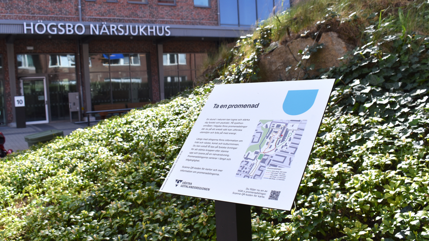 Skylt som visar information om promenadslingor. I bakgrunden entrén till Högsbo närsjukhus.