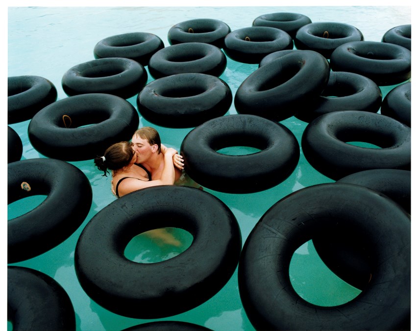 Två personer som kysser varandra i en pool full med stora, svarta badringar