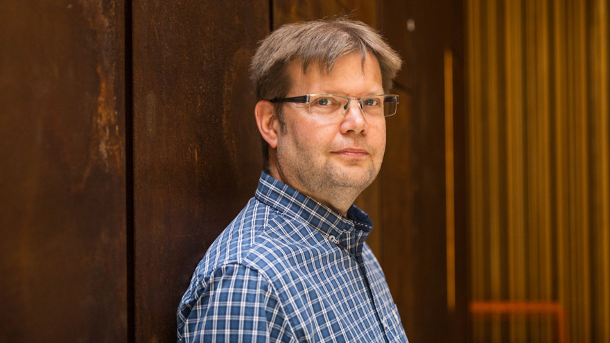Peder Wollinger är i medelåldern, han bär glasögon och är klädd i en blårutig skjorta. Han har kortklippt brunt hår, lite skäggstubb och ser in i kameran med allvarlig min.