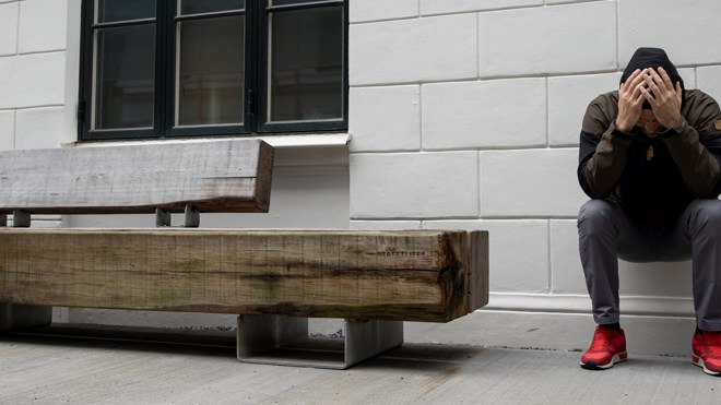 Man sitter lutad mot en vägg och håller händerna för ansiktet.