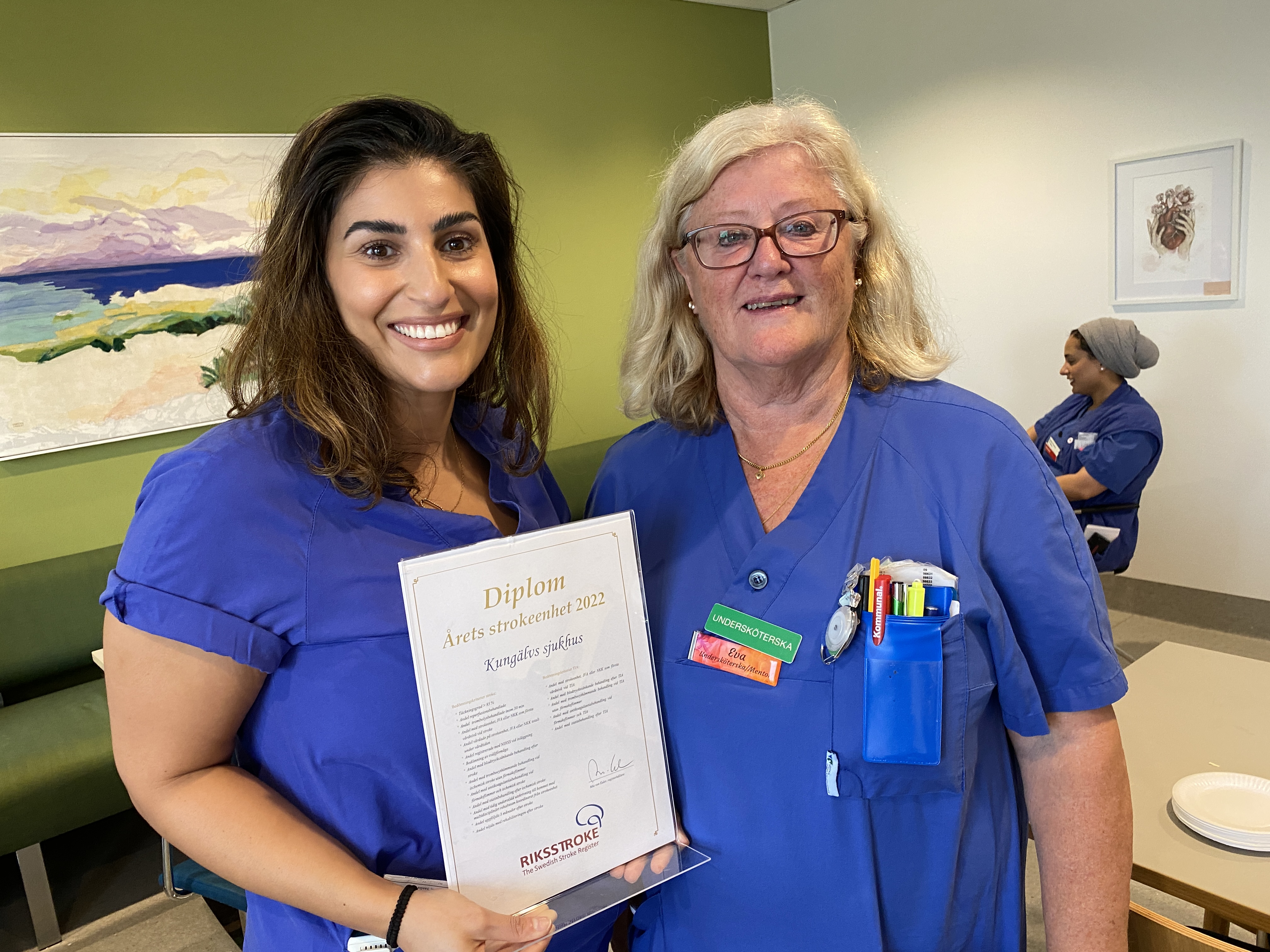 Två leende vårdpersonal håller diplom för Årets strokeenhet.