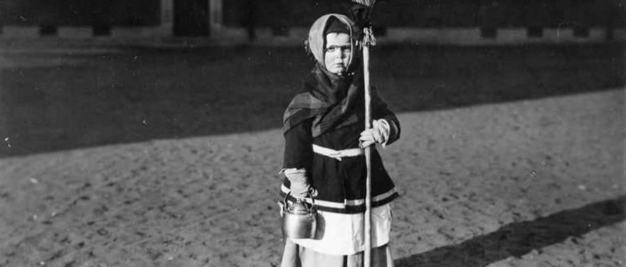 En liten påskkärring håller en kvast och en kaffekittel, svartvit bild