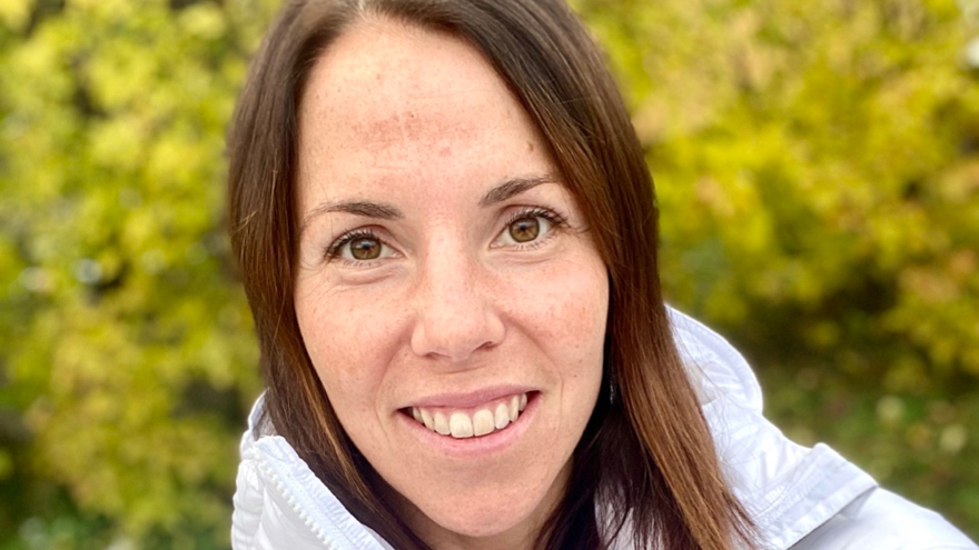 Charlotte Kalla har mörkbrunt rakt hår till axlarna. Hennes ögon är bruna och hon ler på bilden. I bakgrunden syns grönska och hon är klädd i en vit jacka.