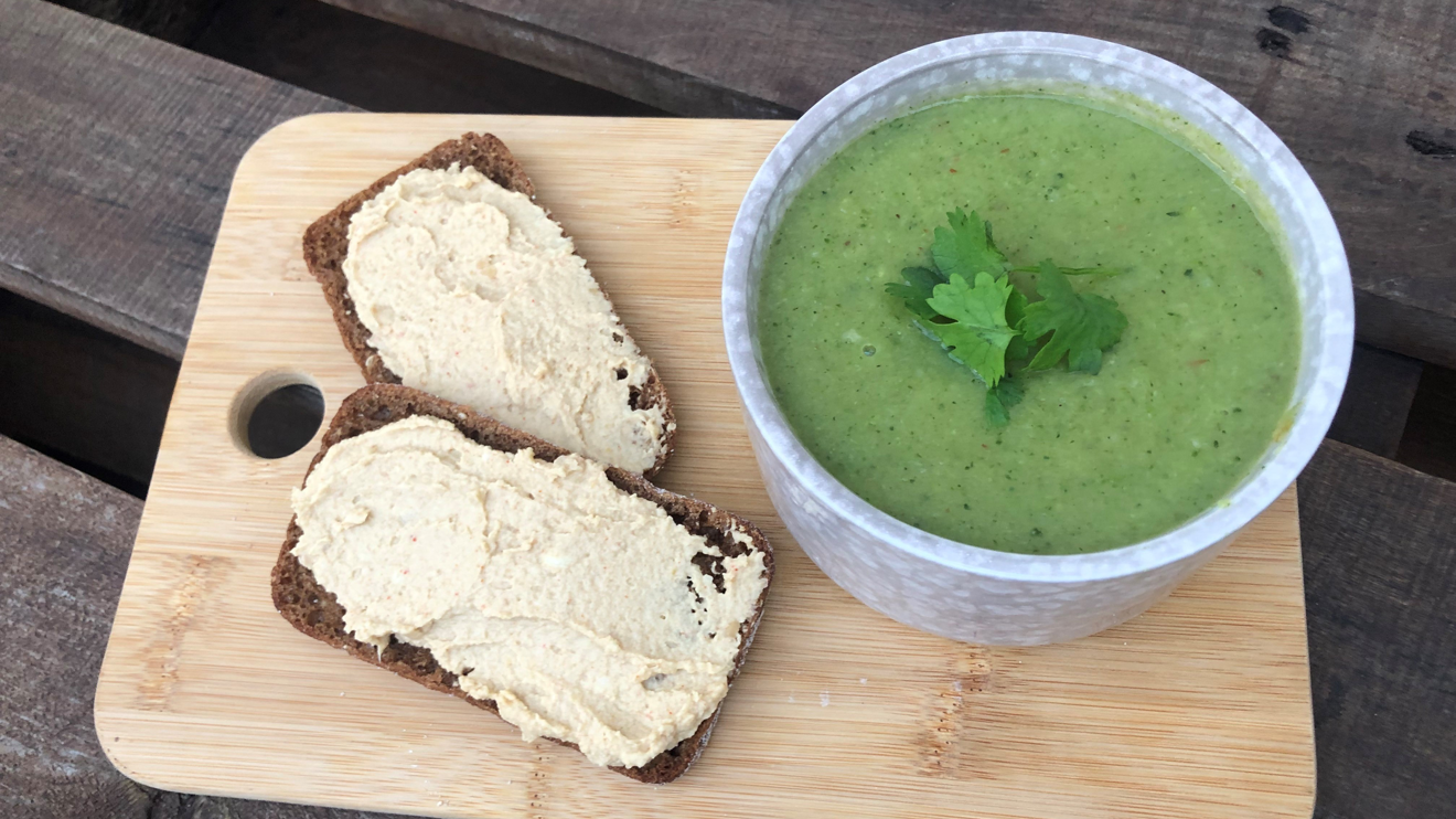 En grön soppa i en skål med två halvor fullkornsbröd med hummus