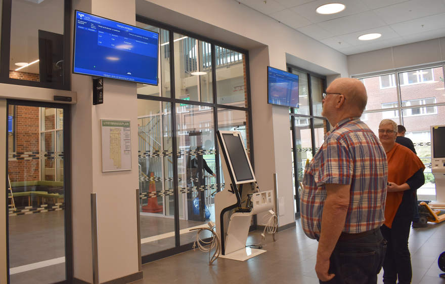 Man i rutig skjorta tittar på en informationsskärm på väggen.