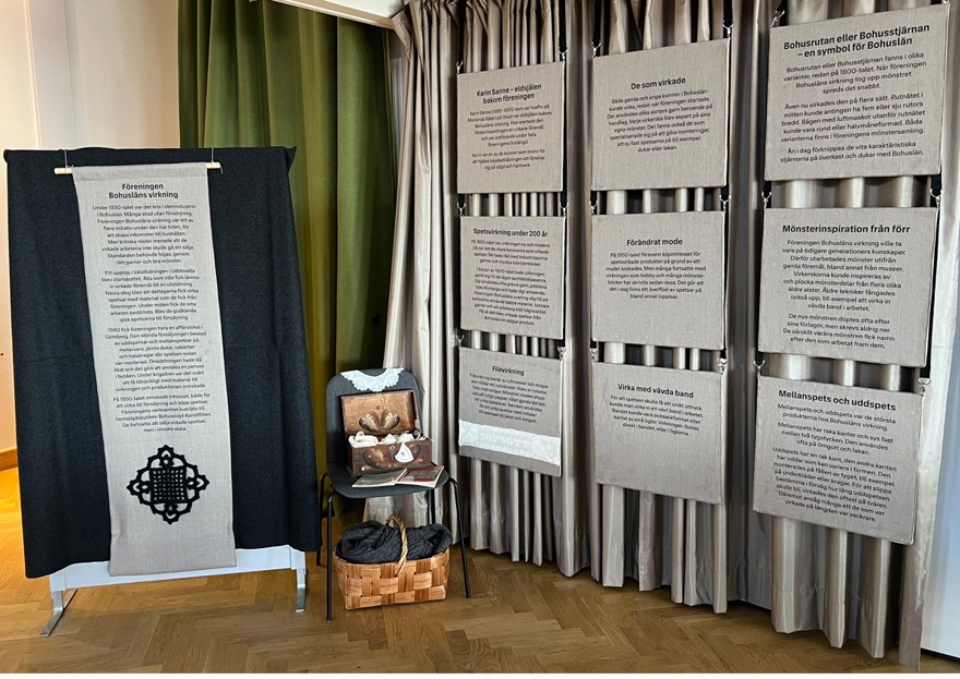 Utställning bestående av informationsskyltar i oblekt linne med svart tryck samt en stol med ett träskrin fyllt av spetsar.