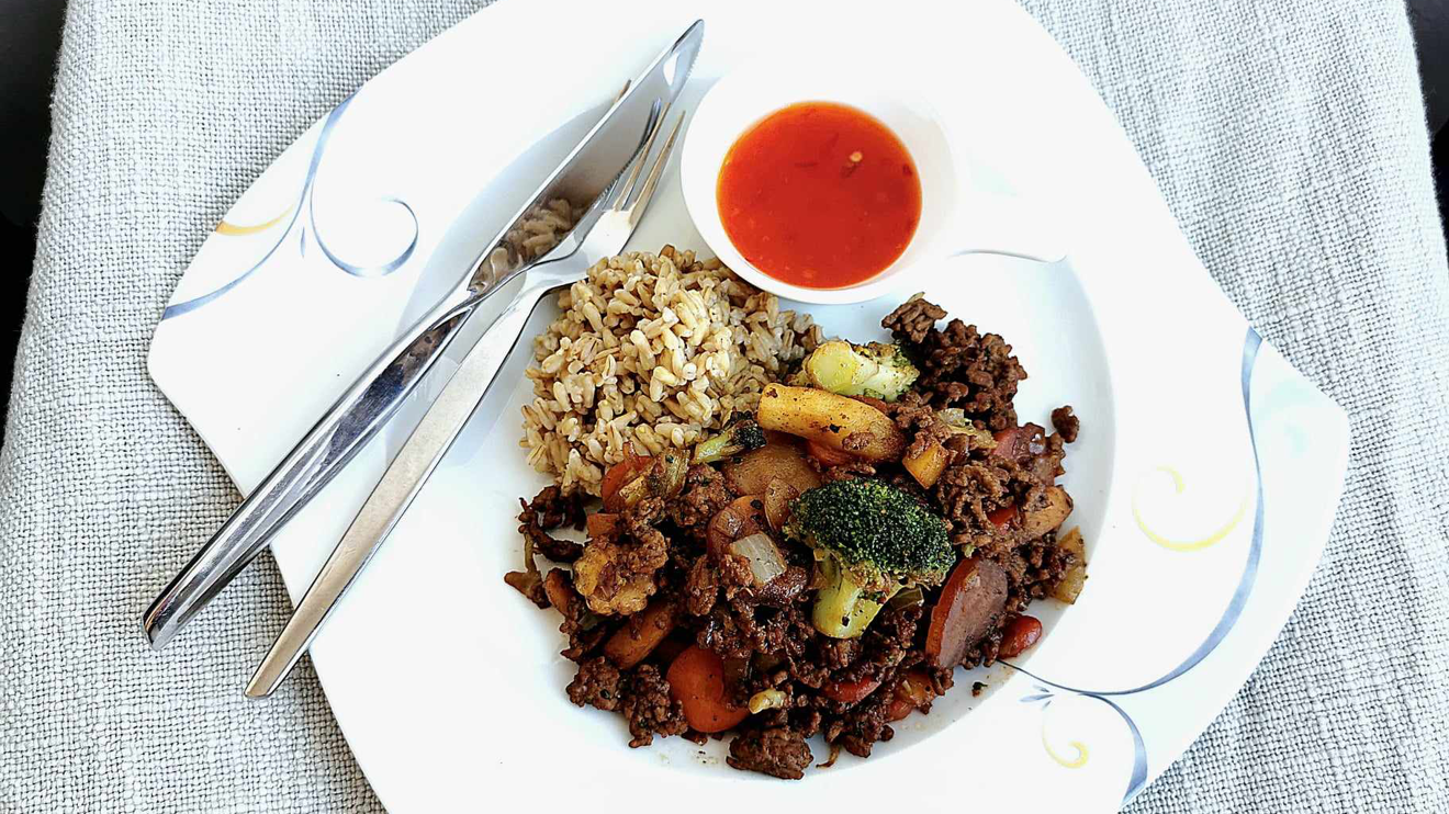 Köttfärsgryta med wokgrönsaker och havreris på en vit tallrik och bestick