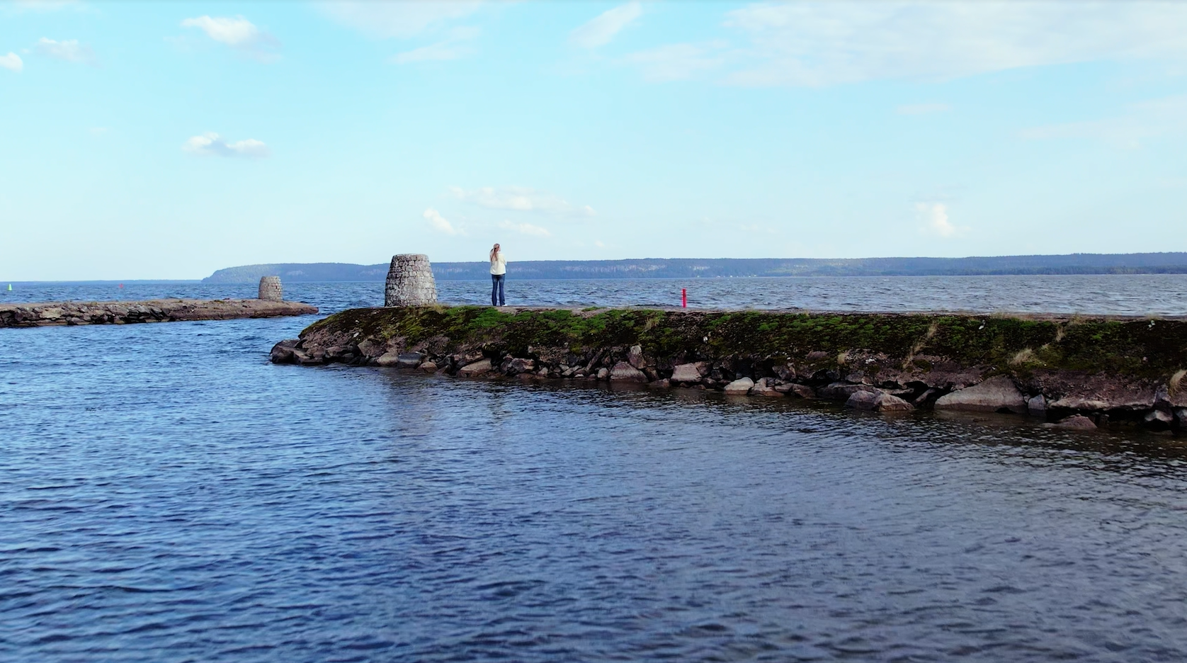 En kvinna står på en pir i Vänern och blickar ut över landskapet