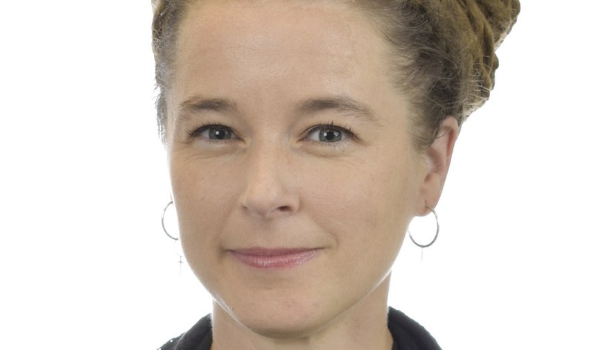 Kvinna, cirka 40 år. Brunt, uppsatt hår. Tunna silverringar i öronen