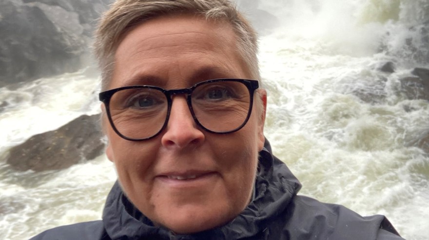 Kvinna, kort hår, glasögon. Står framför ett vattenfall