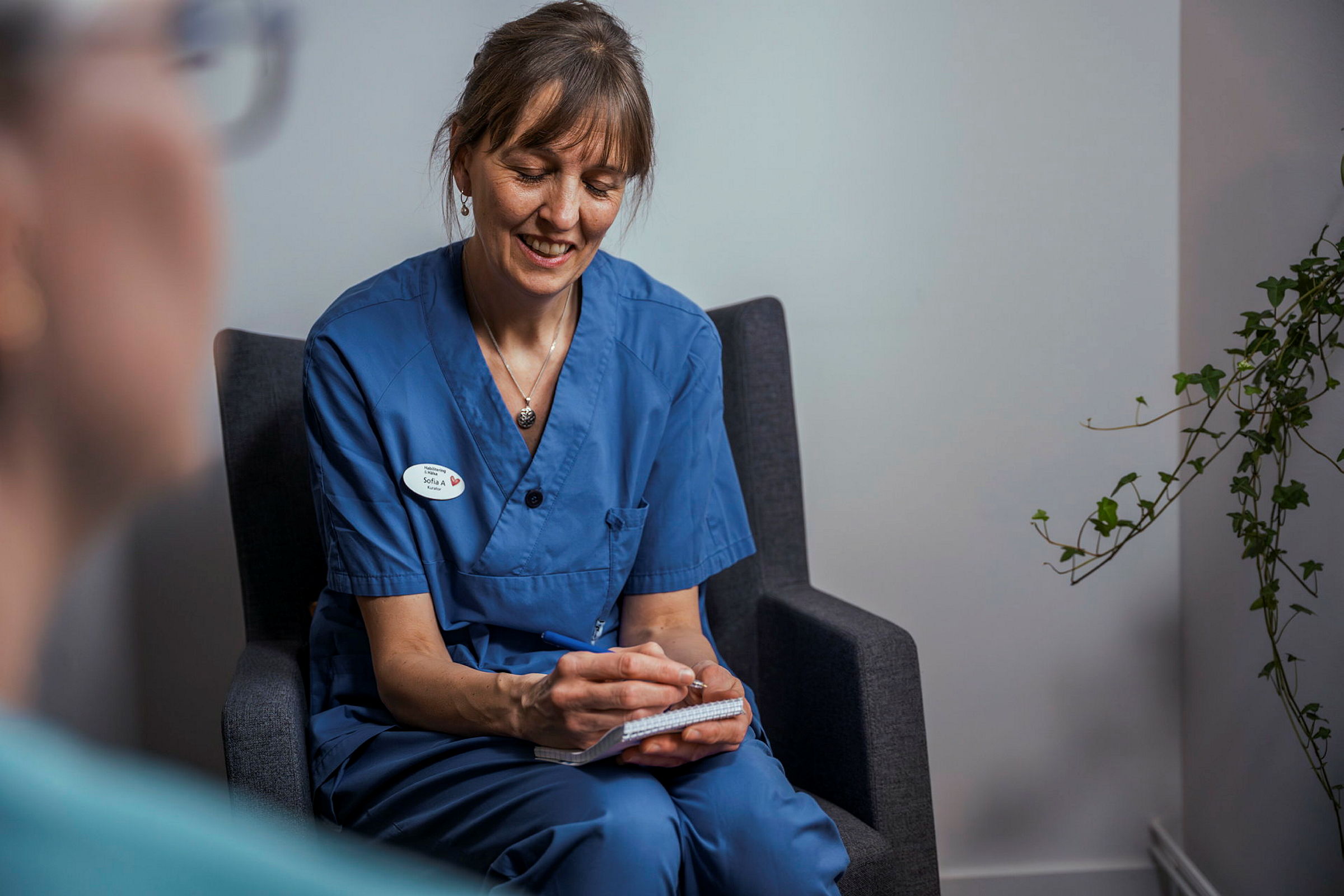 Behandlare i samtal med patient. Tar anteckningar i ett block. 