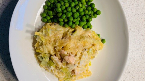 En gul gratäng ligger på en vit tallrik tillsammans med gröna ärtor