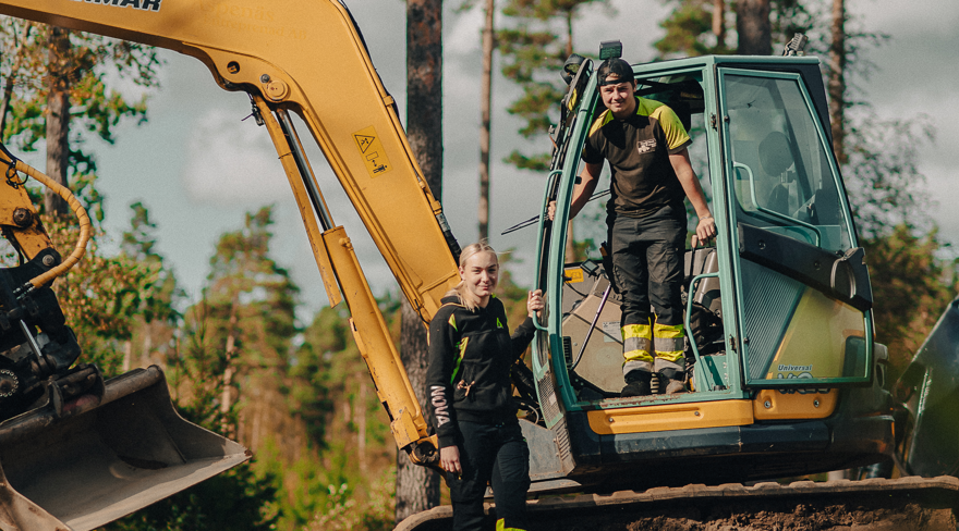 Two students standing with an excavator.