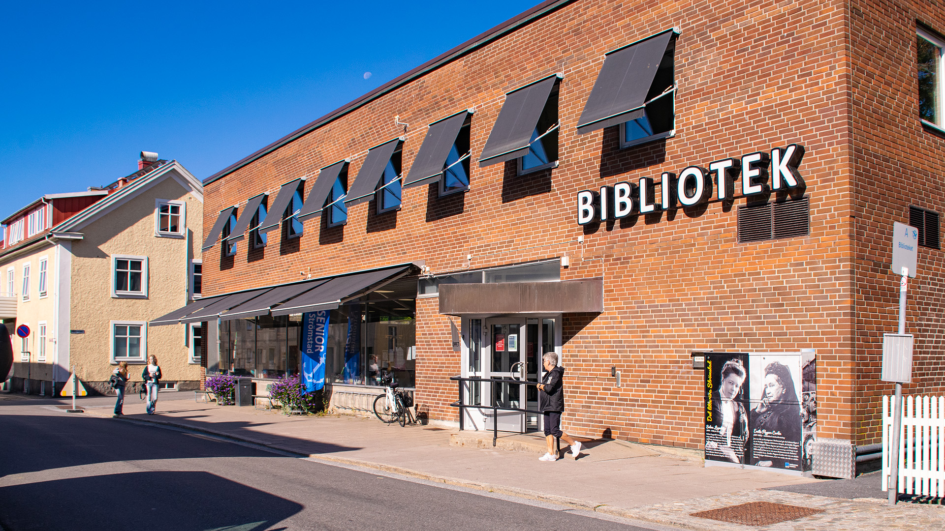 Stadsbiblioteket i Strömstad är en tegelbyggnad i två våningar. På huset står ordet BIBLIOTEK, samtliga fönster har sina svarta markiser nere den här soliga dagen i september. Längre bort på gatan står ett ljusgult rappat äldre tvåvåningshus, ett par unga tjejer går förbi och en kvinna har just gått ut från biblioteket.