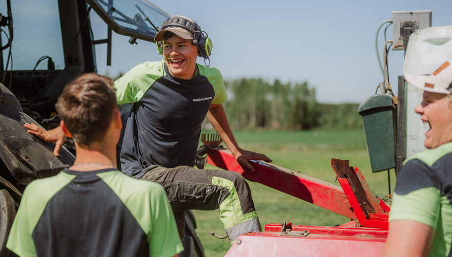 Tre elever står vid traktor vända mot varandra och skrattar