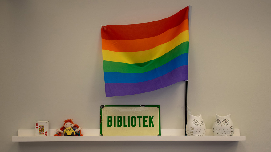 På en liten vägghylla står en regnbågsflagga och en skylt med texten Bibliotek.