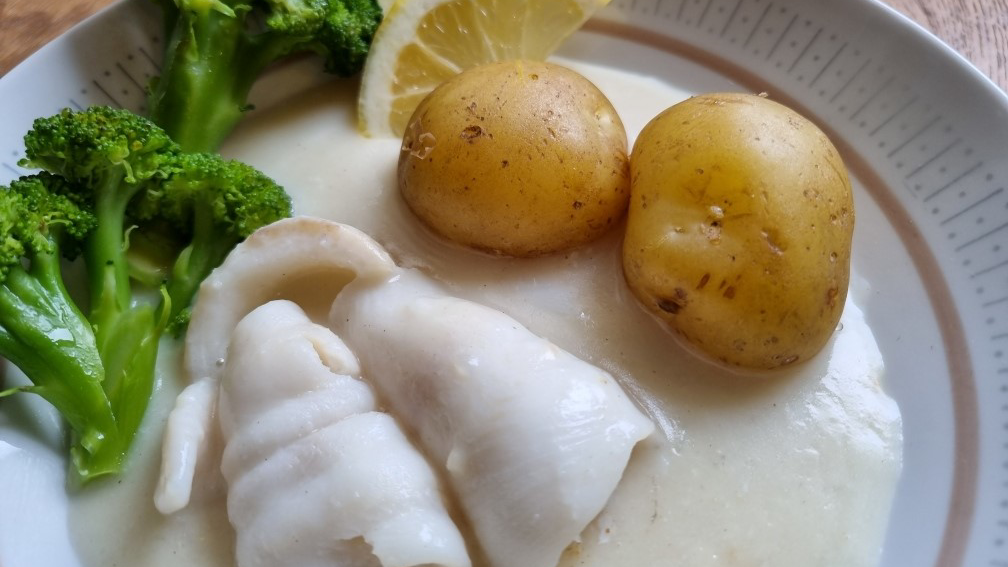 Kokt fisk i citronsås med potatis och proccoli på en vit tallrik