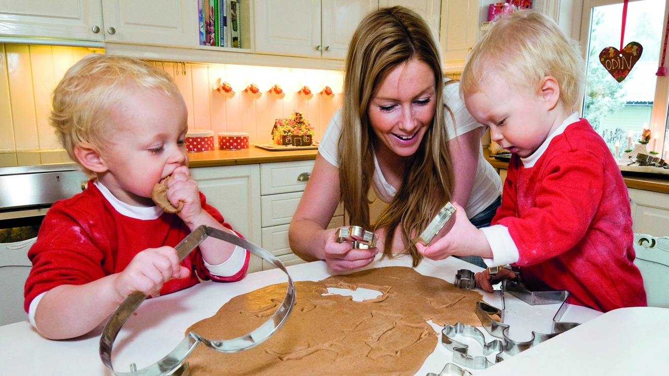 Mamma med två små barn, som är utklädda till tomtar bakar.