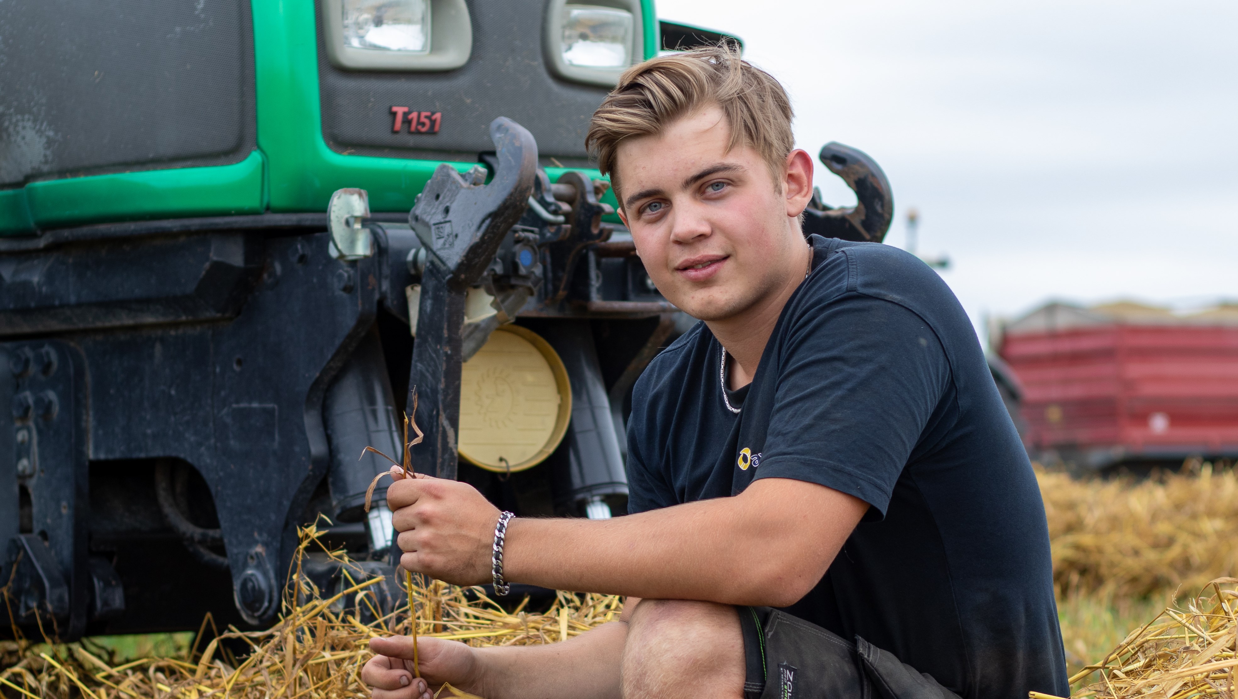 Elev sitter ned bredvid traktor i nyslagen halm