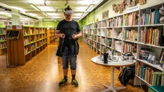 Bibliotekarie Lars Flemming testar VR inför Game On på Kinna bibliotek. Han står med VR-mask inne i biblioteksrummet, har en kontroll i varje hand. Han är klädd i jeansshorts och en svart t-shirt.