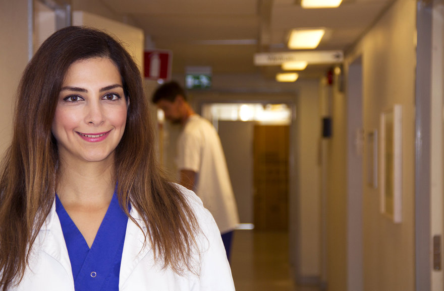 Leende kvinna i sjukvårdskläder i en korridor.