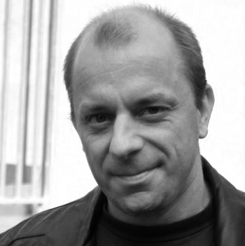 Svartbit bild på man med läderjacka och litet leende.