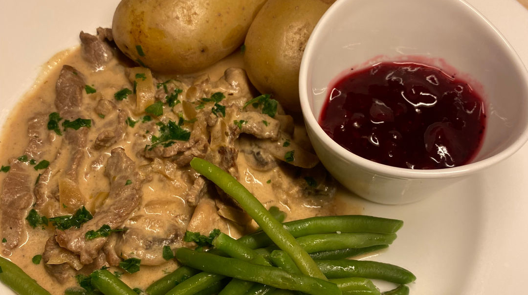 lövbiff, potatis, haricot verts och  lingonsylt på en vit tallrik