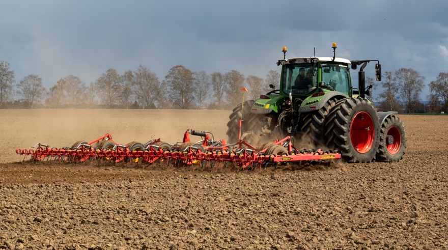 Grön traktor harvar på öppet fält