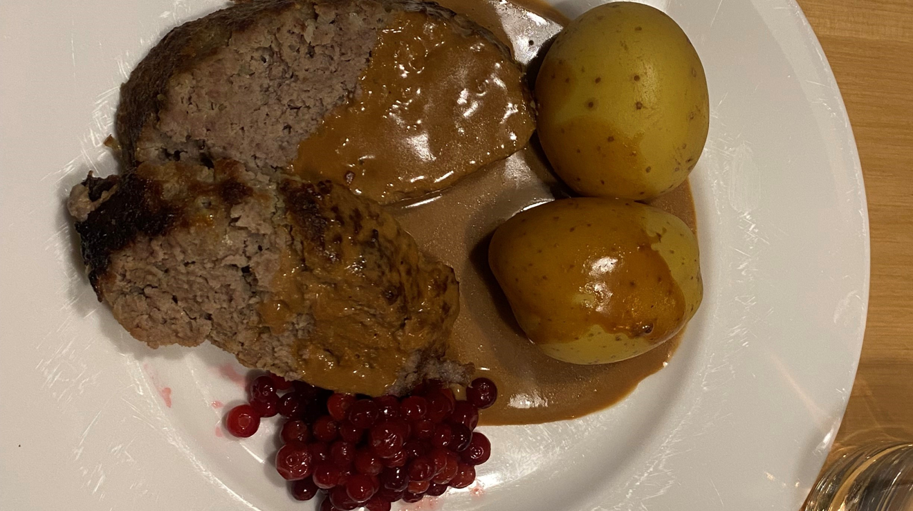 Köttfärslimpa med potatis, lingon och brunsås på en vit tallrik