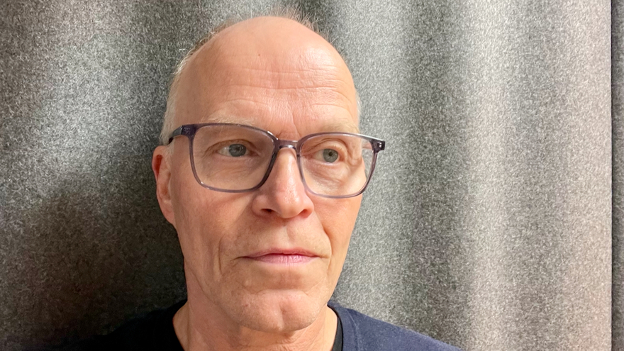 Kurt Levlin är i 60-årsåldern. Han bär glasögon och har vitt kortklippt hår. Han står mot en grå vägg.