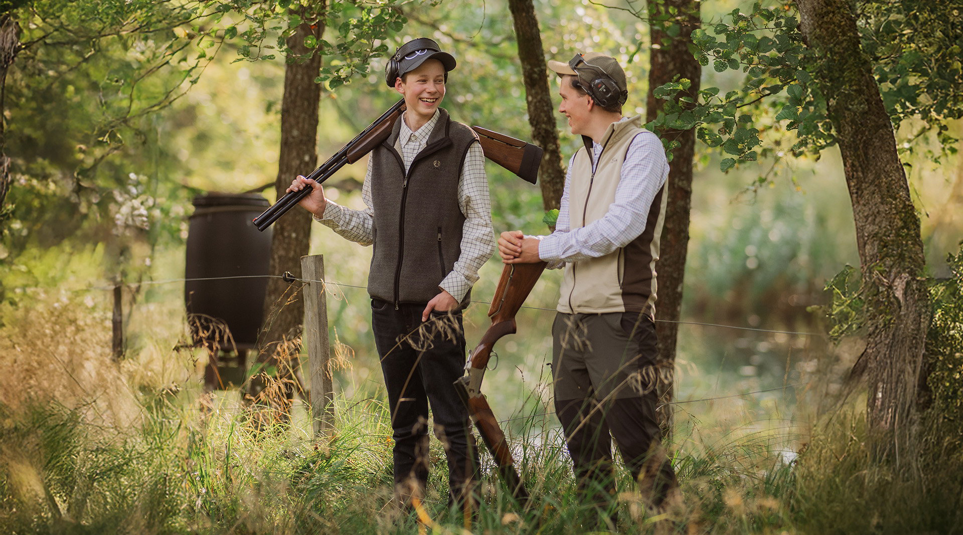 Two hunting students are standing with rifles slung over their shoulders, talking to each other.