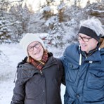 Pensionärspar med snötäckta träd i bakgrunden