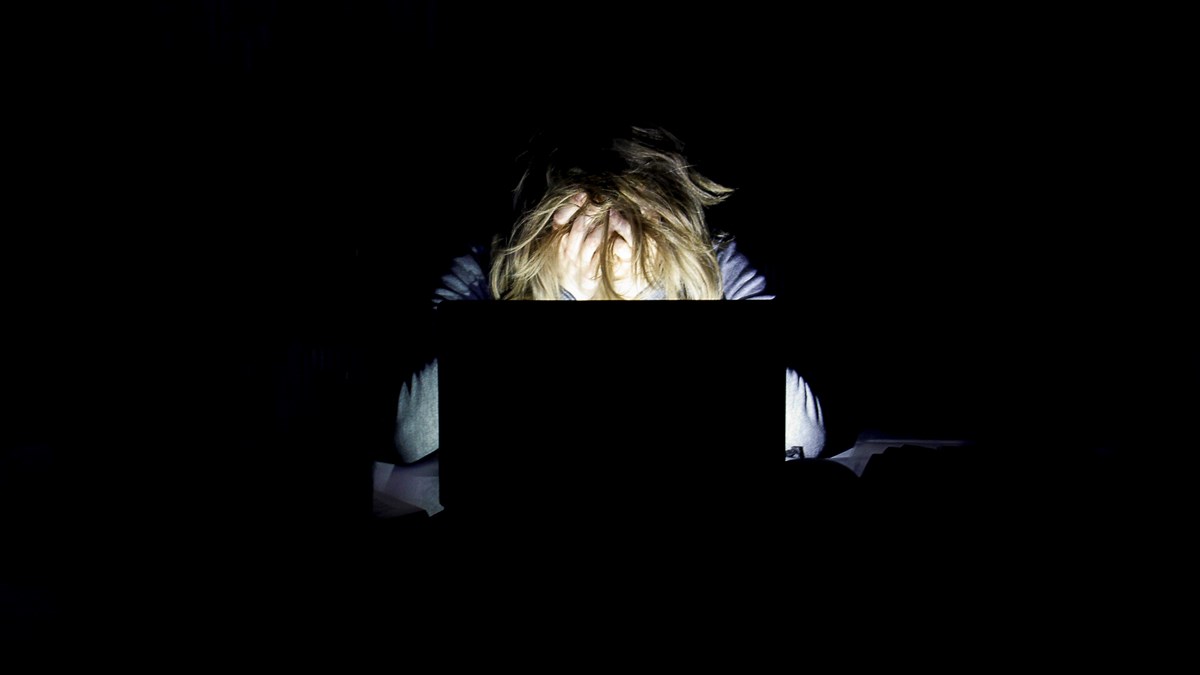 En person sitter i mörkret och arbetar vid datorn.