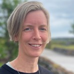 Katarina Nyström står utomhus, håret blåser och himlen är blå.