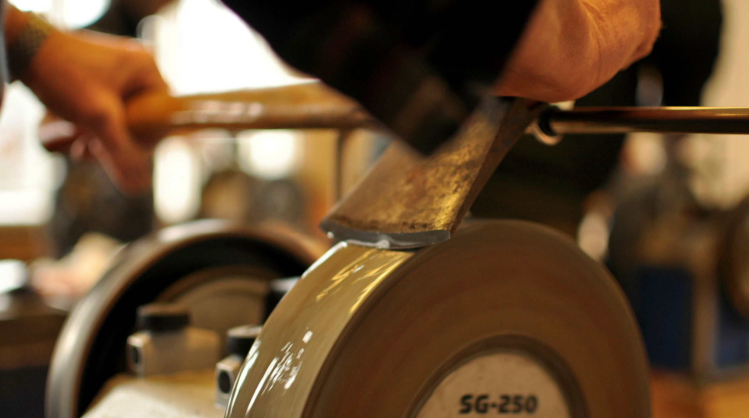 Händer som håller en yxa mot en slipsten