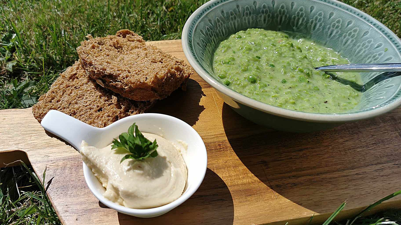 Grön ärtsoppa med fullkornsbröd och hummus på en skärbräda i gräset