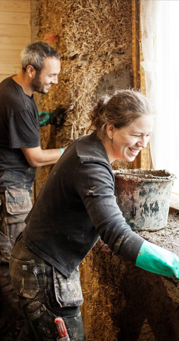Daniel och Karolina lerklinar halmbalsväggarna vid en fönsteröppning
