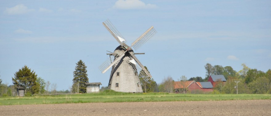 Väderkvarn i Mellbydalen. En grå kvarn med låga byggnader i bakgrunden.