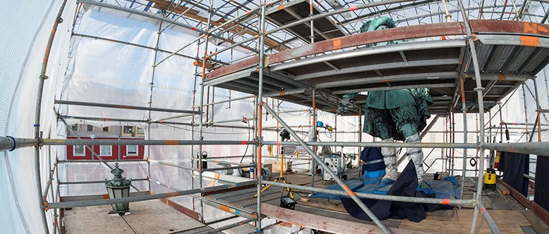 Bilden visar ett virrvarr av byggnadsställningar.Mitt bland byggnadsställningarna syns statyn av Gustav II Adolf. Vid foten av sockeln sitter en person och arbetar. På ett ställe sticker en gatlykta upp.