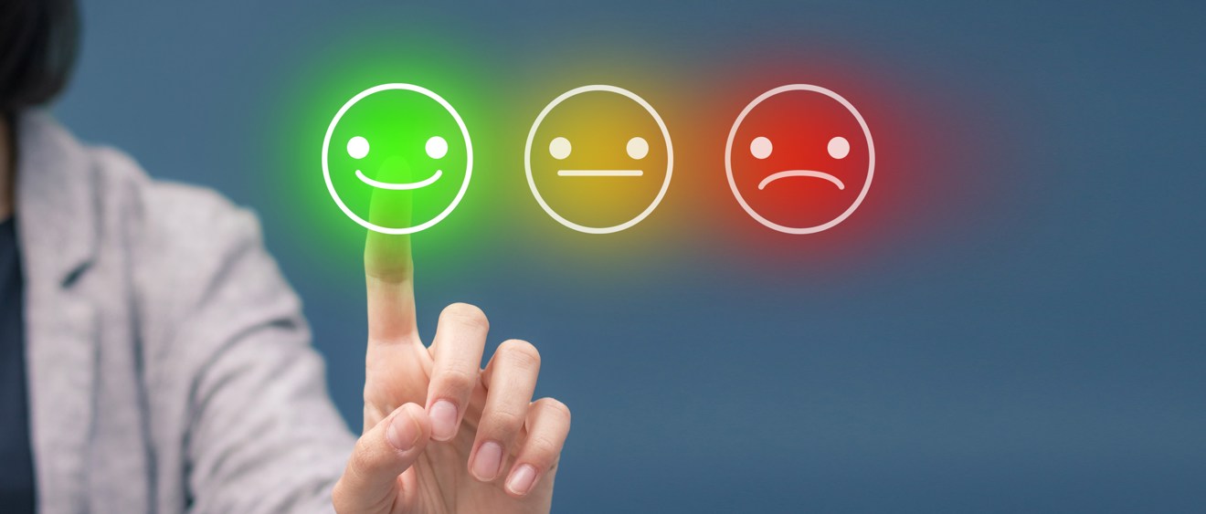 Närbild av en person som trycker på en grön, glad smiley. Bredvid den gröna smileyn finns en gul, neutral smiley och en röd, ledsen smiley.