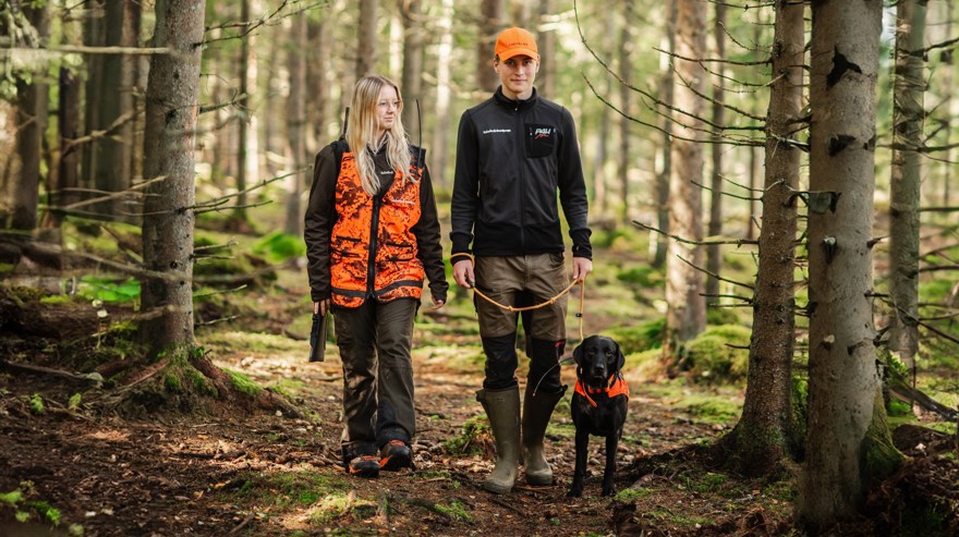 Två jaktelever med hund promenerar i skogen